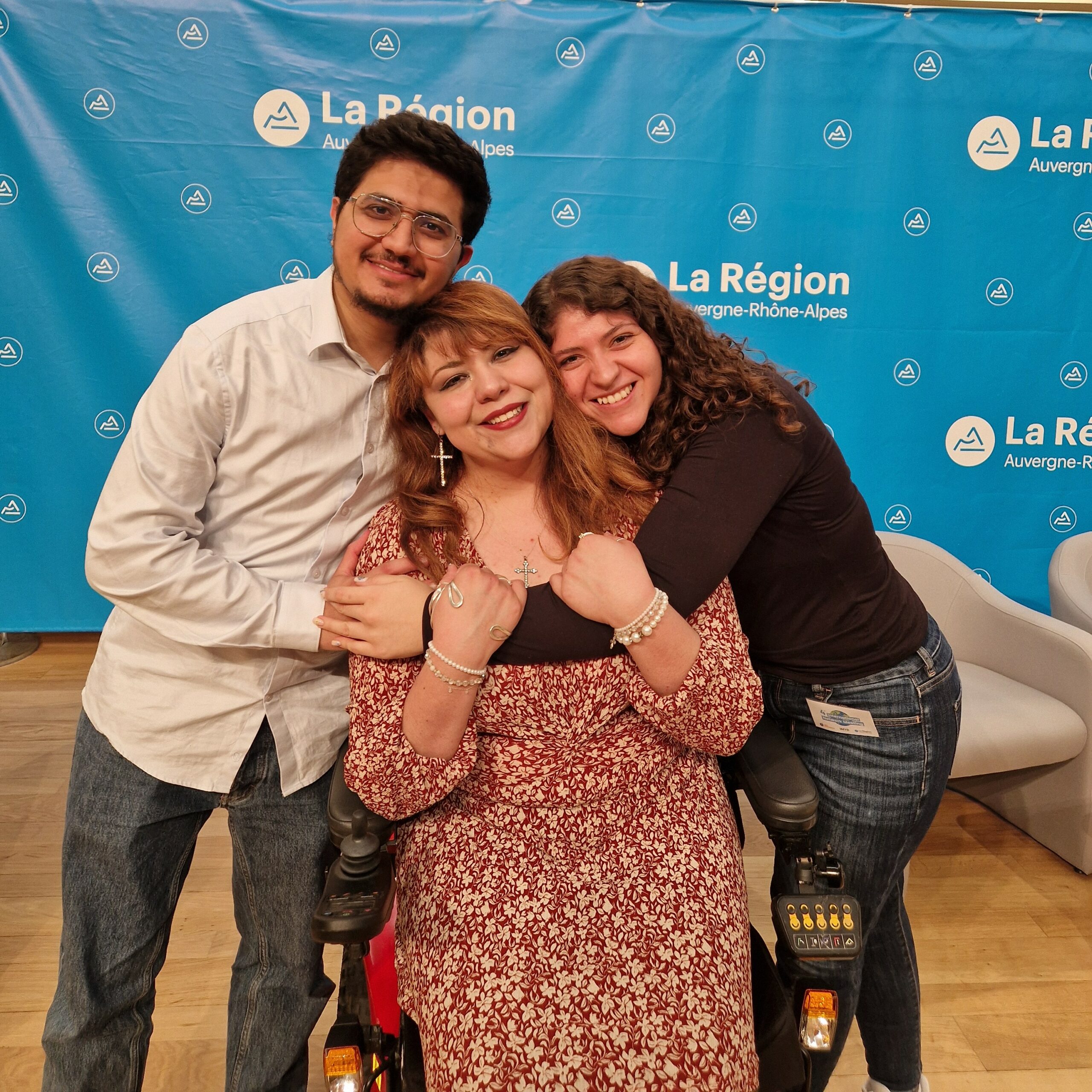 Three persons hugging eachother smiling and looking at the camera.